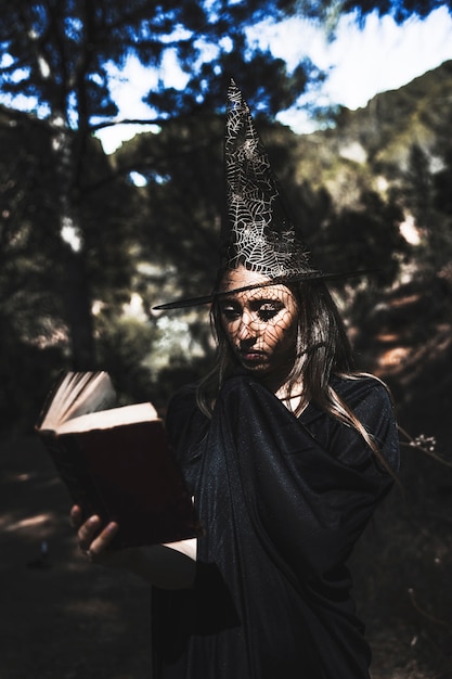 Free photo young woman in wizard costume reading book in forest