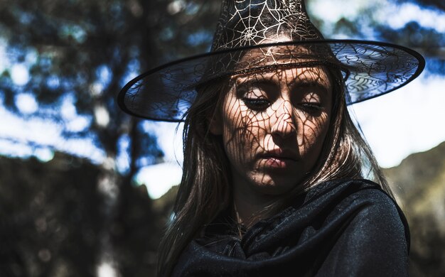 Young woman in wizard hat and cloak looking down in forest