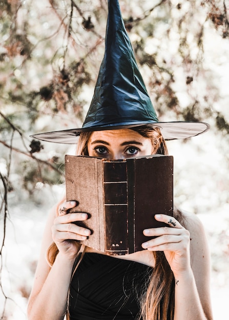 Free photo young woman in wizard hat closing mouth with book