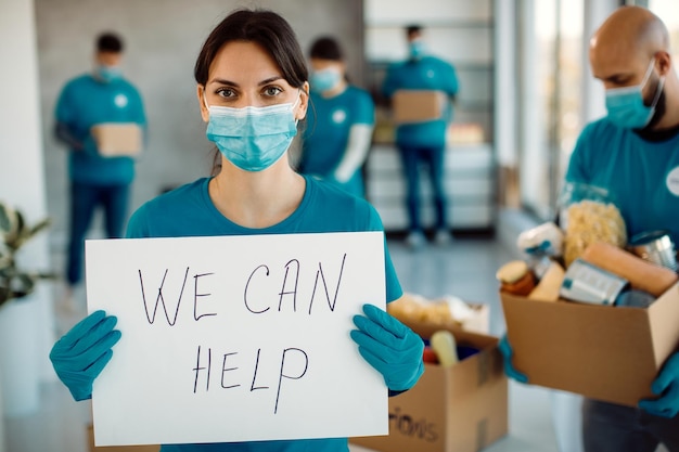 Young woman working as volunteer and holding a placard with 'we can help' inscription