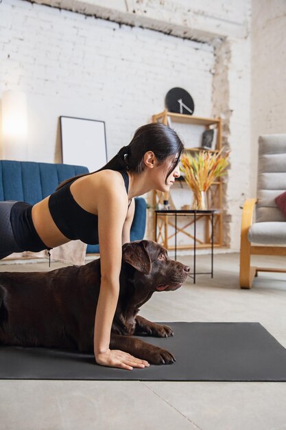 Young woman working out at home. Yoga exercises with the dog