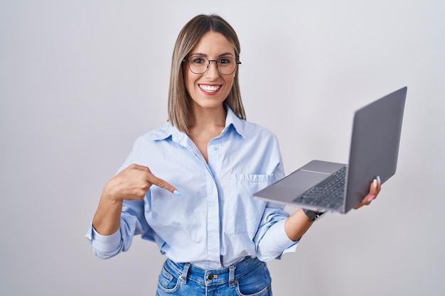 Young woman working using computer laptop looking confident with smile on face pointing oneself with fingers proud and happy