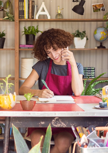 Free photo young woman writing something in her notebook in greenhouse