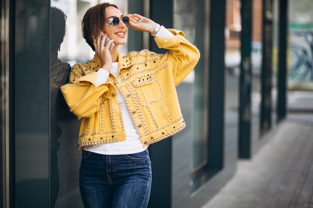 Free photo young woman in yellow jacket using phone outside in the street