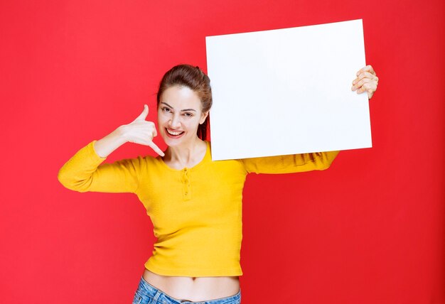 Young woman in yellow shirt holding a square info board and asking for a call