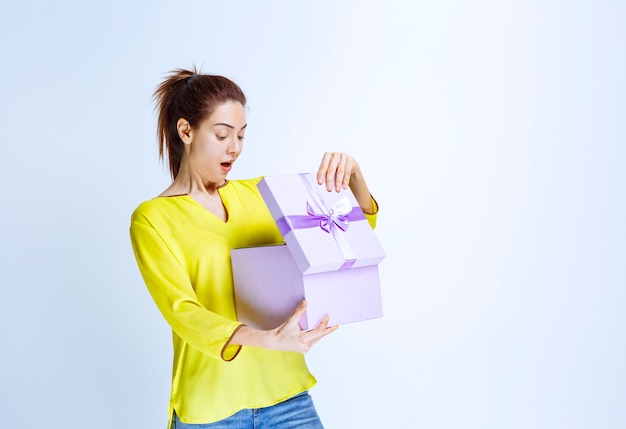 Young woman in yellow shirt opening a violet gift box with surprize