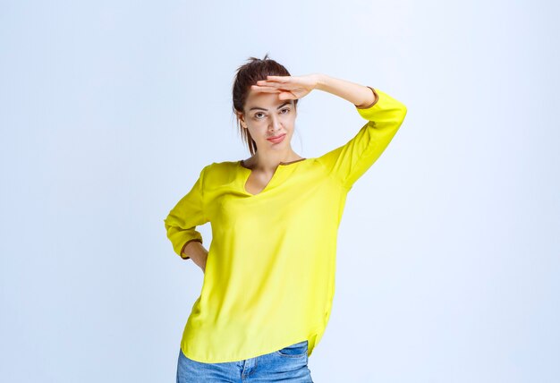 Free Photo young woman in yellow shirt putting hand to forehead and observing ahead