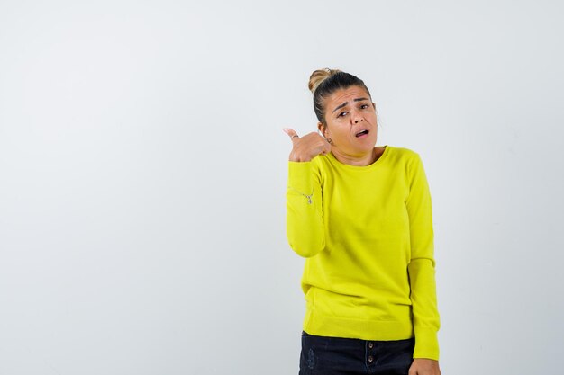 Young woman in yellow sweater and black pants showing call me gesture and looking happy