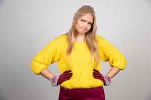 Free photo young woman in yellow sweater and red gloves posing over a gray wall .