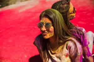 Free photo young women covered in holi colors wearing sunglasses sitting back to back