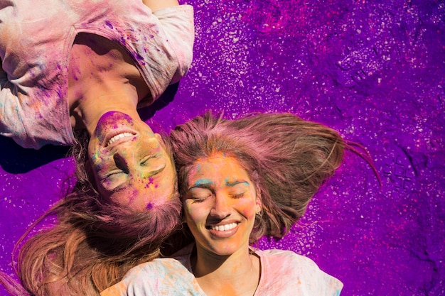 Free photo young women covered with holi powder lying on purple color