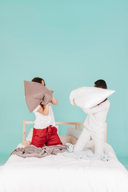 Free photo young women fighting with pillows on bed