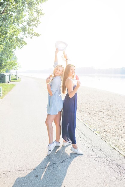 Free photo young women standing back to back enjoying icecream at beach