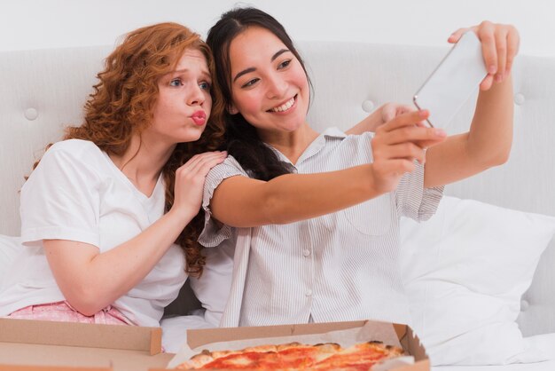 Young women taking selfie while eating pizza