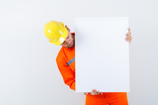 Free photo young worker looking at blank canvas in uniform, helmet and looking focused.