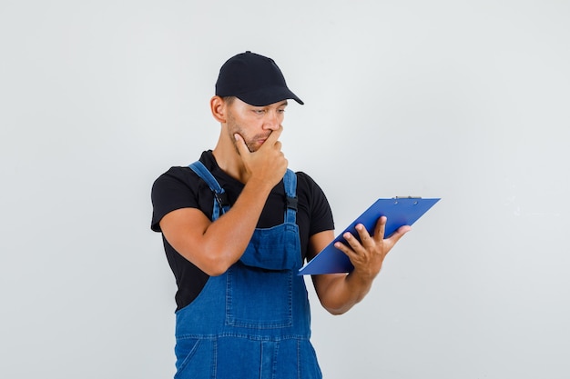 Free photo young worker looking over clipboard in uniform and looking pensive. front view.