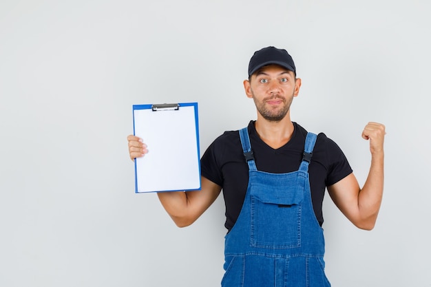 Free Photo young worker pointing back and holding clipboard in uniform front view.