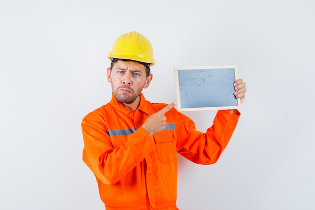 Young worker pointing at blackboard in uniform, helmet.