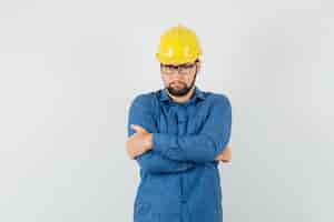 Free photo young worker in shirt, helmet standing with crossed arms and looking serious