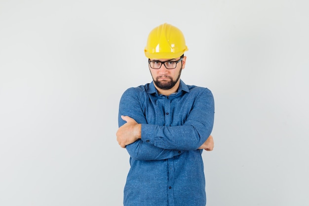 Free Photo young worker in shirt, helmet standing with crossed arms and looking serious