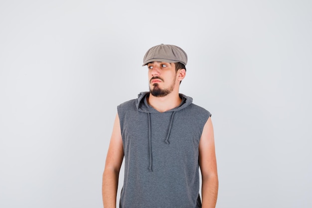 Free photo young worker standing straight, looking away and posing at front in gray t-shirt and cap and looking serious