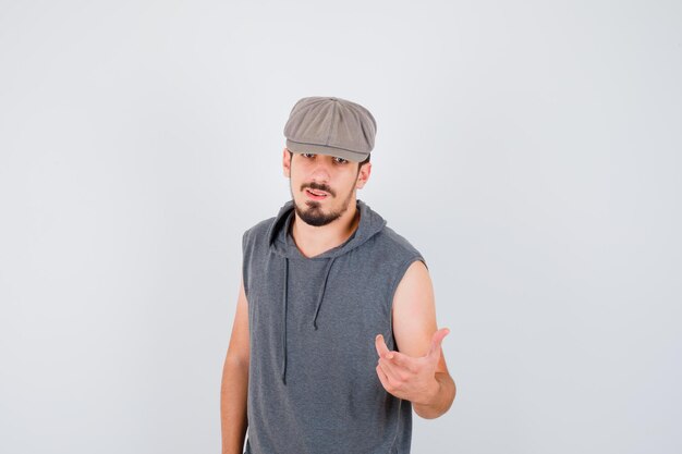 Young worker standing straight and stretching hand toward front in gray t-shirt and cap and looking happy