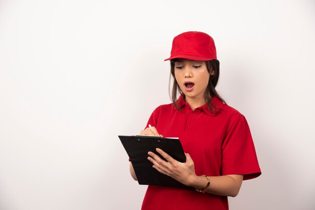 Young worker with red uniform and clipboard on white background.