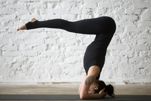 Young yogi attractive woman in headstand pose, white loft backgr