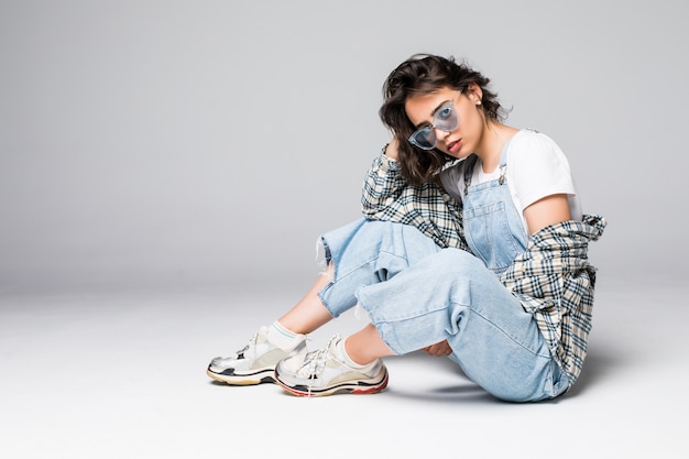 Young young female in casual clothes sitting on the floor posing over grey wall copy space