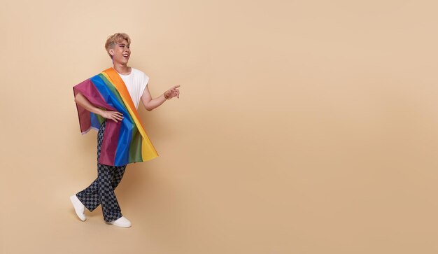 Youth asian transgender LGBT with Rainbow flag on shoulder isolated over nude color background