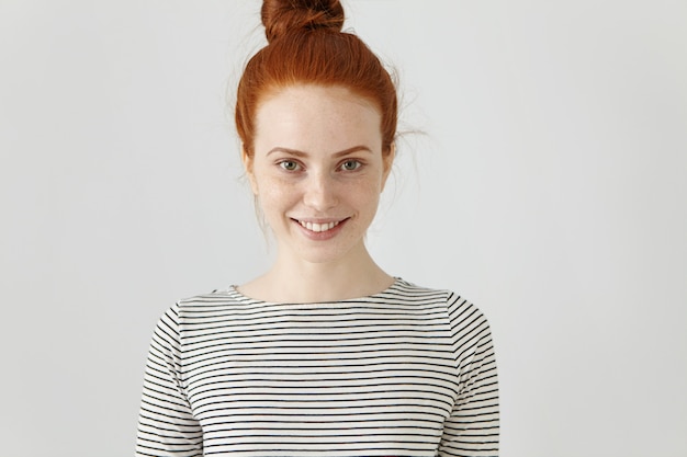 Free photo youth and happiness concept. cheerful carefree red-haired teenage girl with hair bun and freckled clean skin smiling broadly, feeling happy and relaxed while enjoying her leisure time indoors