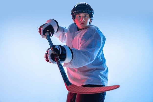 Free photo youth. young male hockey player with the stick on white background in neon light. sportsman wearing equipment and helmet practicing. concept of sport, healthy lifestyle, motion, movement, action.