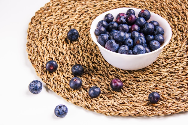 Yummy blueberries in a white round bowl on a white and wicker placemat background. high angle view.