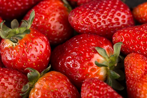 Yummy strawberries red mellow ripe with green leafs on dark desk