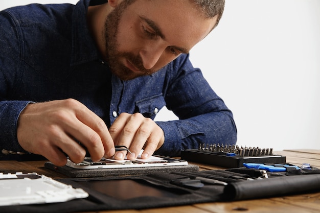 Free photo yung bearded master looks inside disassembled electronic device while repairing it with tools