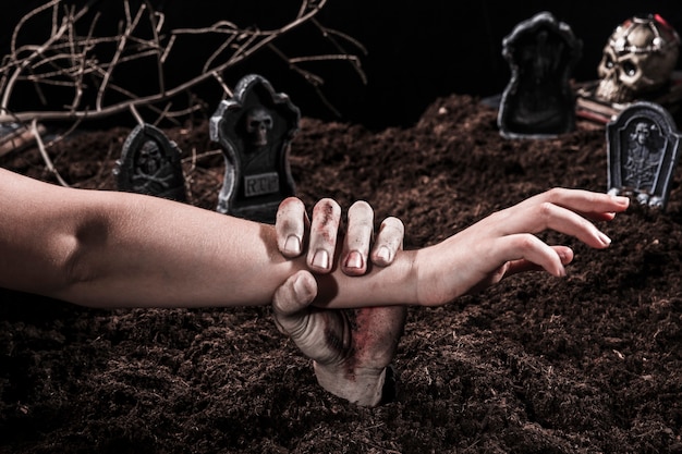 Free Photo zombie hand holding person arm at halloween graveyard