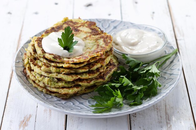 Zucchini fritters with yogurt sauce on white wooden table