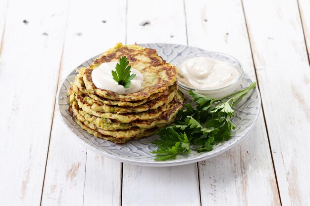 Zucchini fritters with yogurt sauce on white wooden table