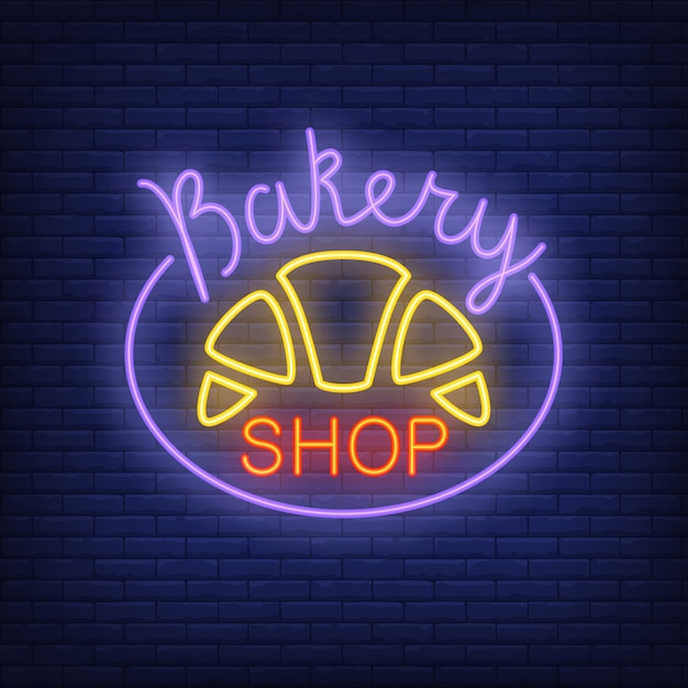 Bakery shop neon sign. Bright croissant on dark blue brick wall. 