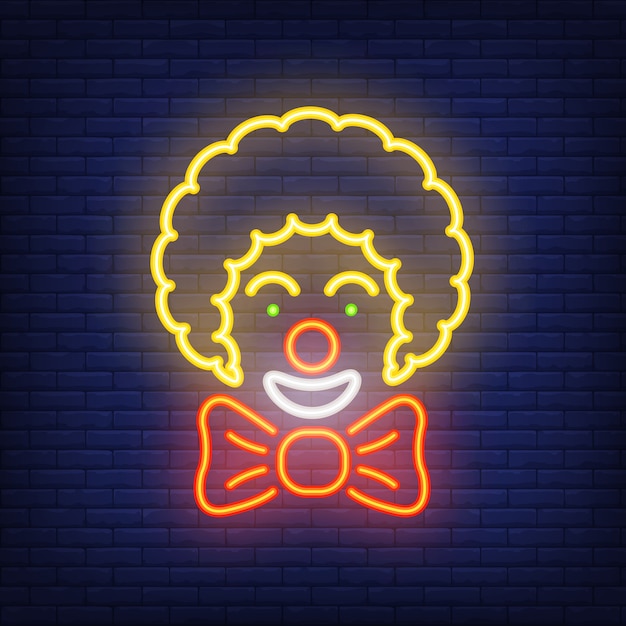 Smiling clown neon icon. Circus artist with big bow on dark brick wall background. 