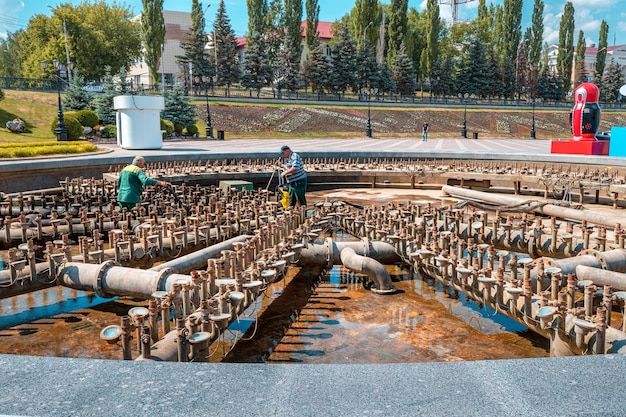 09 June 2021 Ufa Russia Two workers clean and maintain the old fountain in the city park on the square