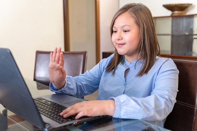 10 year old blonde girl greeting someone at a video conference on a laptop at home