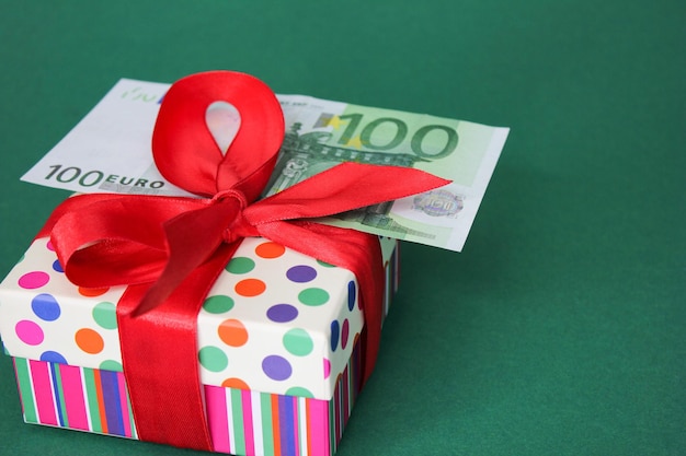 100 Euro banknote on a gift box with a red bow. Green background.