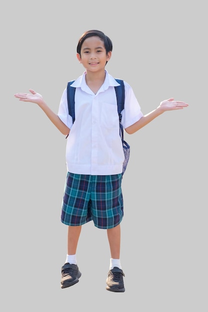 A 10yearold Asian boy in a school uniform is standing with two hands raised and smiling