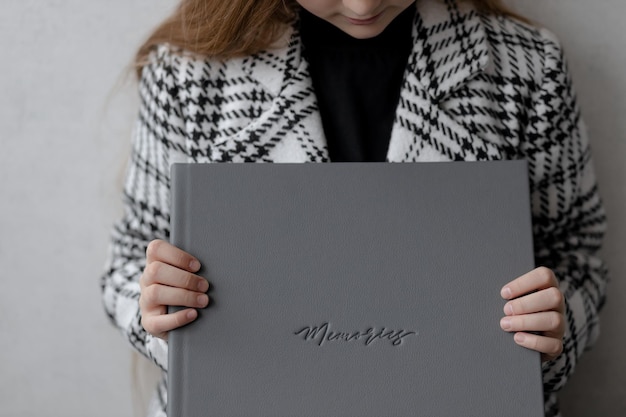 A 10yearold girl is sitting holding a gray leather photo book