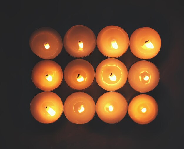 12 burning candles on dark background