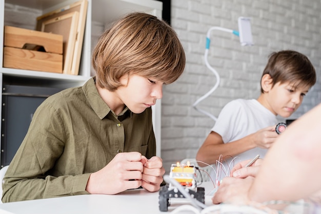 12 year old boy in green shirt constructing a robot car at workshop