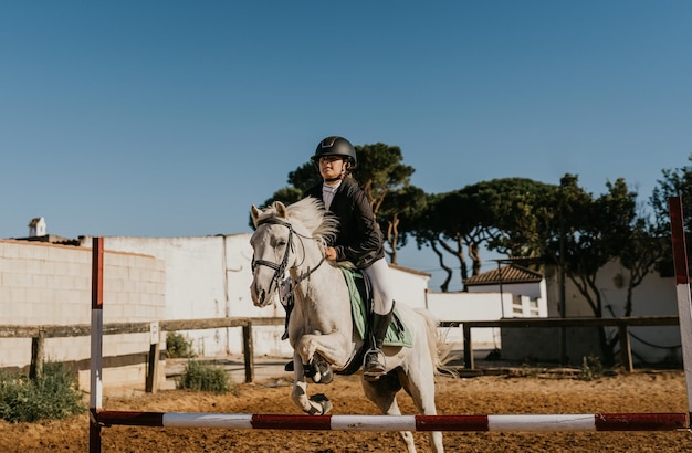 12yearold girl riding a white pony jumps an obstacle at a riding school