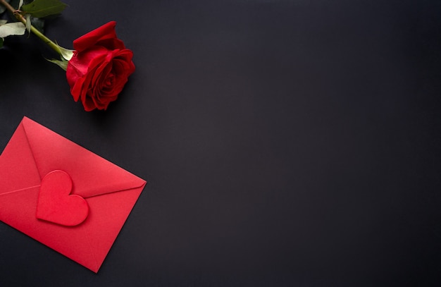 14 Valentines day background. Red flowers of rose and envelop with heart on black background, top view, copy space