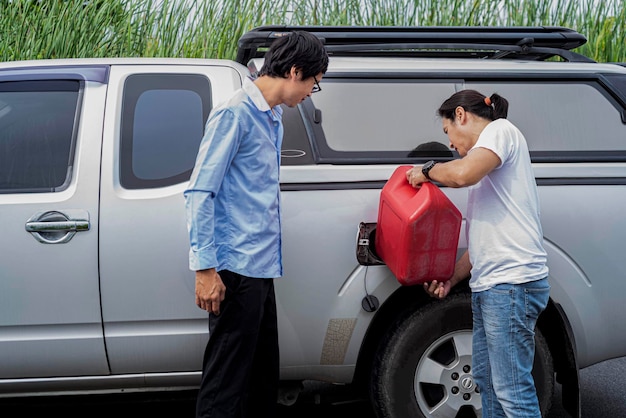 2 Asian man holding a Reserve oil tank To refuel the pickup truck Parked on the roadside